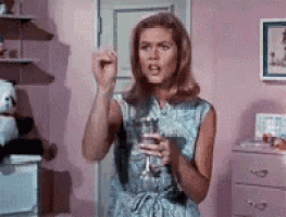 a woman is standing in a pink room holding a glass of wine .