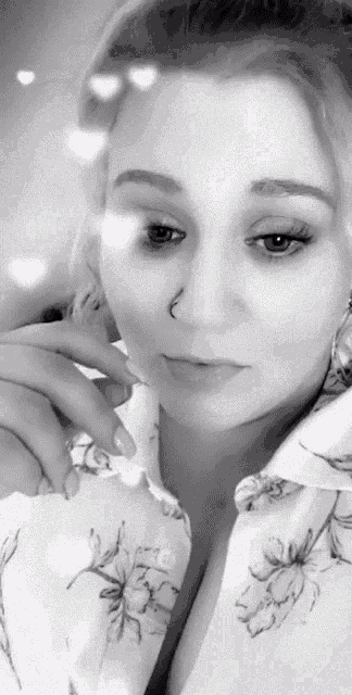 a black and white photo of a woman with a nose ring and a floral shirt .