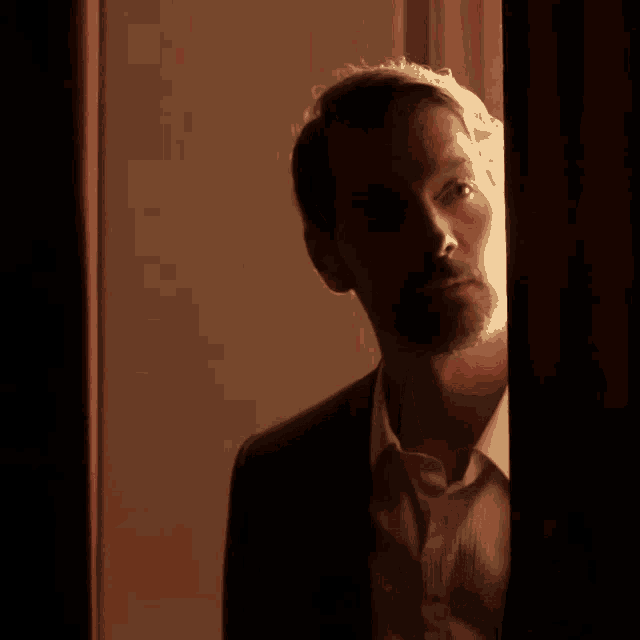a man in a suit and white shirt is looking out of a window