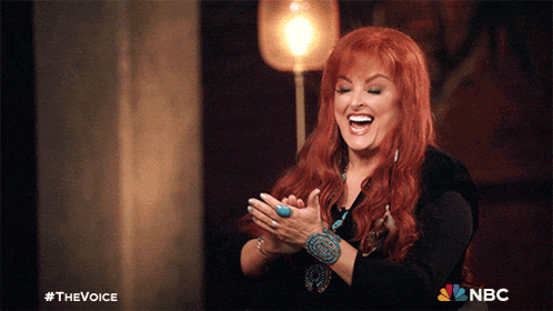 a woman with red hair is smiling and clapping her hands in front of a nbc logo
