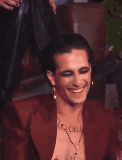 a man with a tattoo on his chest is smiling and wearing a red jacket and earrings .