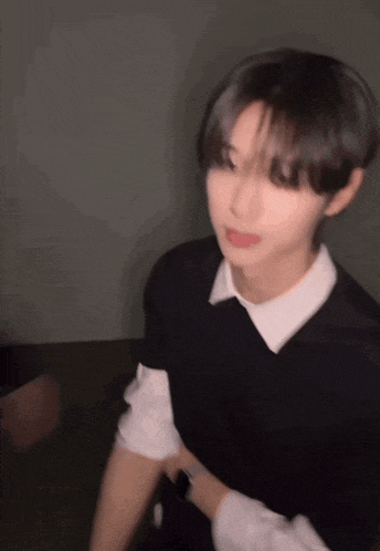 a blurry picture of a young man with short hair wearing a black vest and a white shirt .