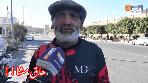 a man with a beard wearing a md shirt talks into a microphone