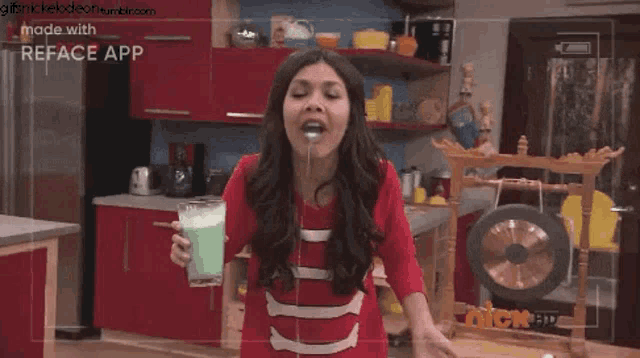 a woman is drinking a green drink in a kitchen with a reface app on her phone .