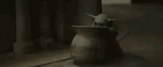 a baby yoda is drinking from a clay pot .