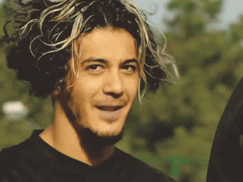 a young man with curly hair and a beard smiles