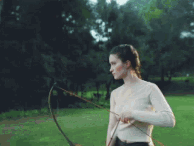 a woman holds a bow and arrow in a field