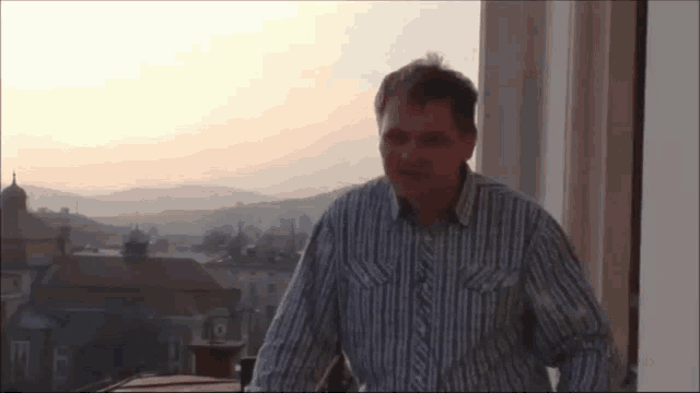 a man wearing a striped shirt stands in front of a window