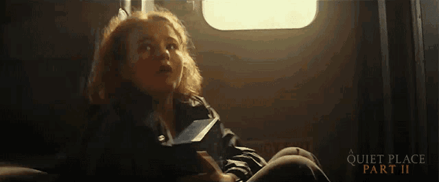 a movie poster for quiet place part ii shows a woman sitting in a dark room
