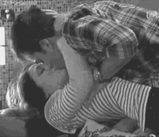 a black and white photo of a man and a woman kissing .