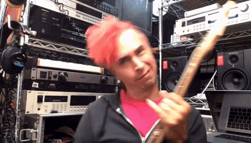 a man with pink hair is playing a guitar in front of a rack of electronics including an akai