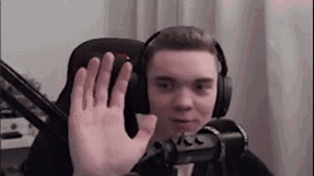 a young man wearing headphones is sitting in front of a microphone and waving .