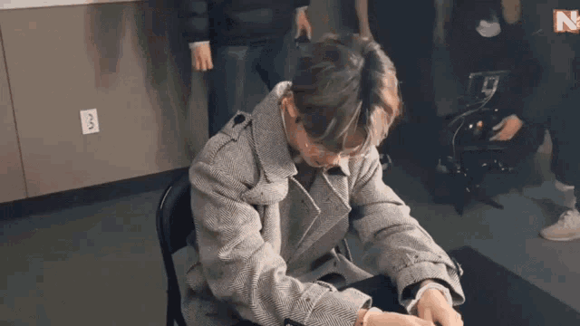a man in a trench coat is sitting in a chair with his head down .