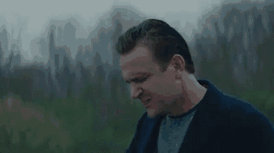 a man in a blue jacket is standing in a field looking down .