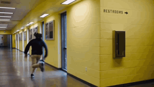 a person running down a hallway with a sign that says restrooms on it