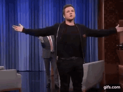 a man is standing in front of a couch with his arms outstretched on a stage .