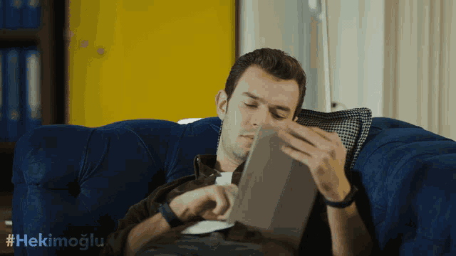 a man is laying on a blue couch reading a tablet