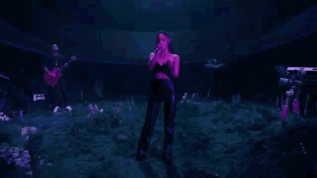 ariana grande is singing into a microphone on a stage in a dark room .