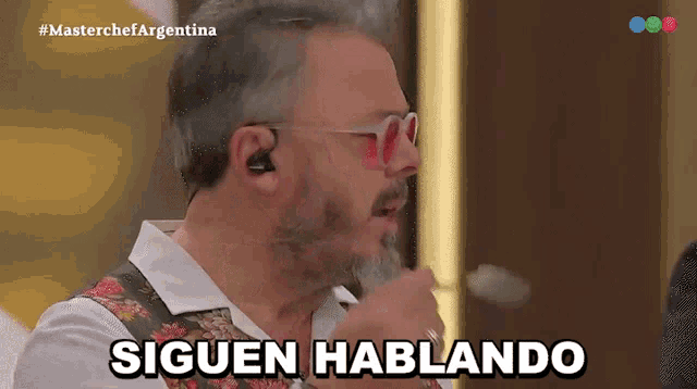 a man with a beard and sunglasses says " siguen hablando " in spanish