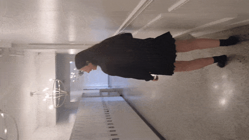 a woman in a black skirt is standing in a hallway with a white wall