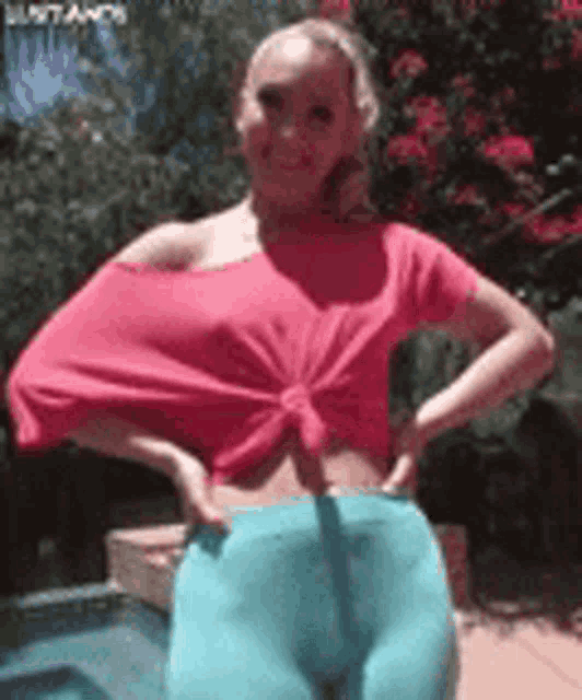 a woman in a pink top and blue pants is standing with her hands on her hips .