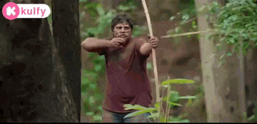 a man in a red shirt is holding a bow and arrow in a forest .