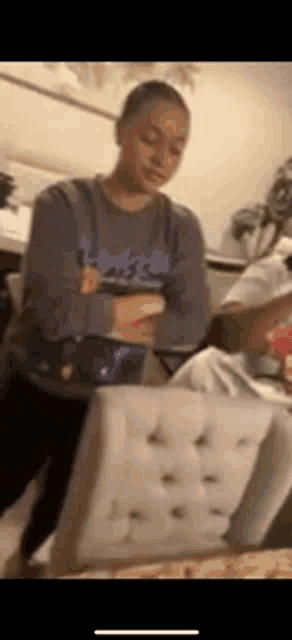 a woman in a gray sweatshirt is standing next to a white chair .