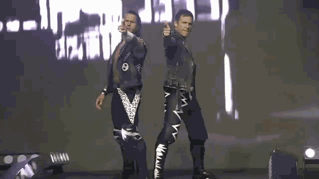 two men are standing next to each other in front of a large screen with the word death on it