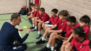 a man is talking to a group of young boys wearing red shirts that say ccc