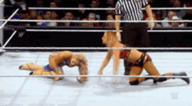 two women are wrestling in a ring while a referee watches