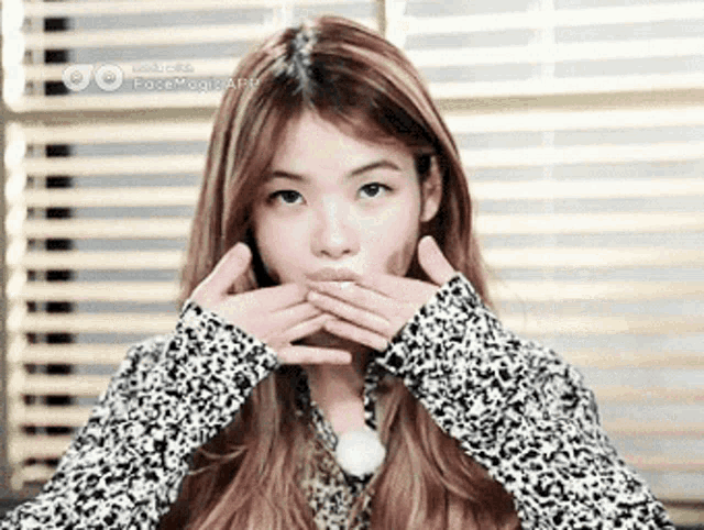 a woman covering her mouth with her hands while wearing a sweater