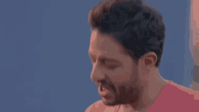 a man with a beard is wearing a pink shirt and making a face .