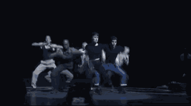 a group of people are dancing together on a stage in a dark room .