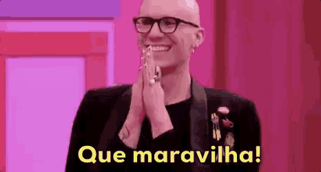 a bald man wearing glasses and a black suit is smiling and clapping his hands .