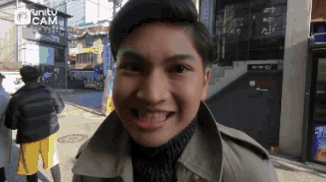 a man in a trench coat is smiling in front of a sign that says unity cam