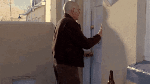 an older man is knocking on a door with a bottle of beer in front of him .