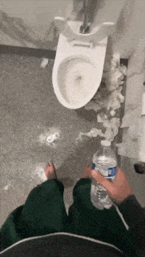 a person holding a bottle of aquafina water in a bathroom