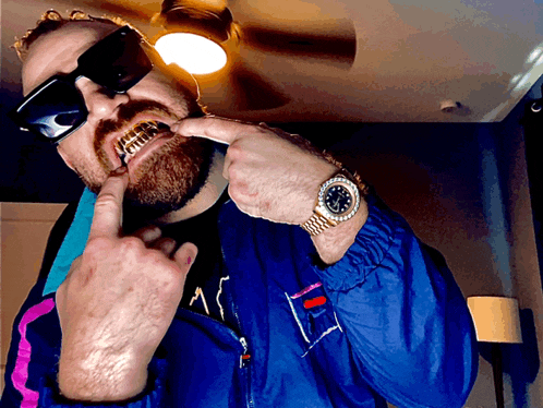 a man wearing sunglasses and a blue jacket has a gold watch on his wrist