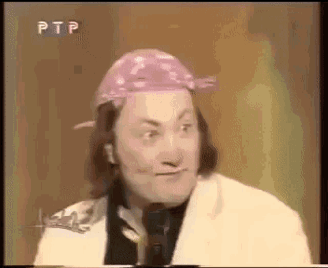 a man wearing a purple bandana and a white suit is talking into a microphone .