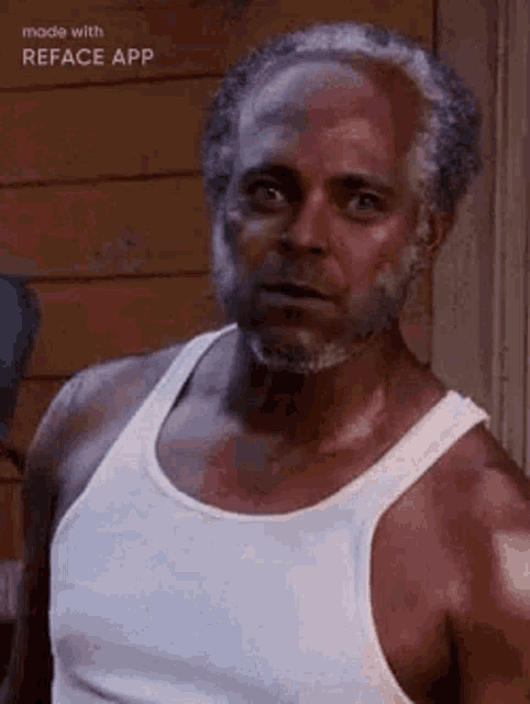 an older man with a beard is wearing a white tank top and looking at the camera .