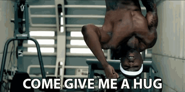 a shirtless man is upside down in a gym with the words come give me a hug below him