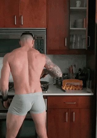 a shirtless man in boxer shorts is standing in a kitchen preparing food .