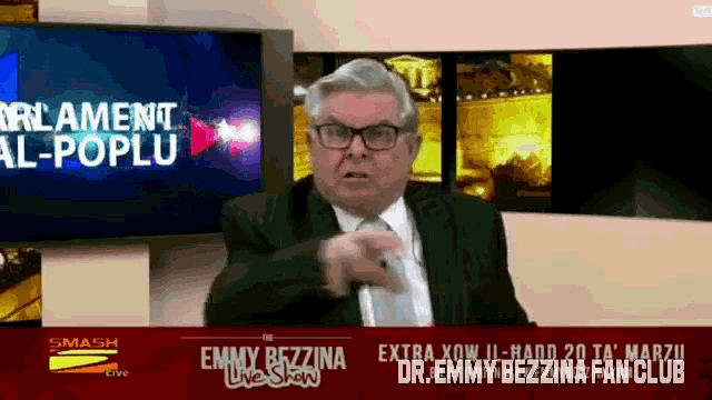 a man in a suit and tie is pointing in front of a screen that says smash live
