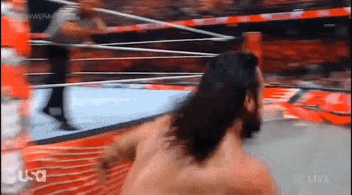 a man with long hair is wrestling in a ring with a referee in the background .
