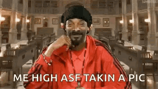 snoop dogg is wearing a red jacket and a black hat and smiling while taking a picture .