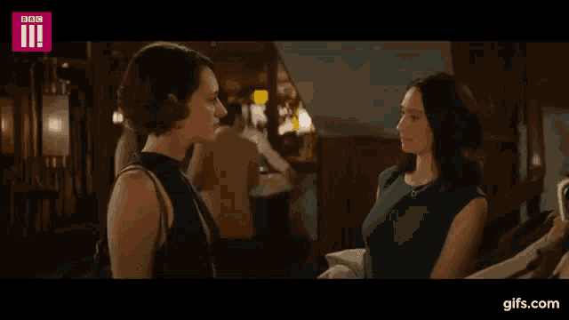 two women are standing next to each other in a room talking to each other .