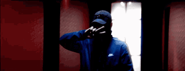a man wearing a blue nike jacket and a black hat is making a peace sign