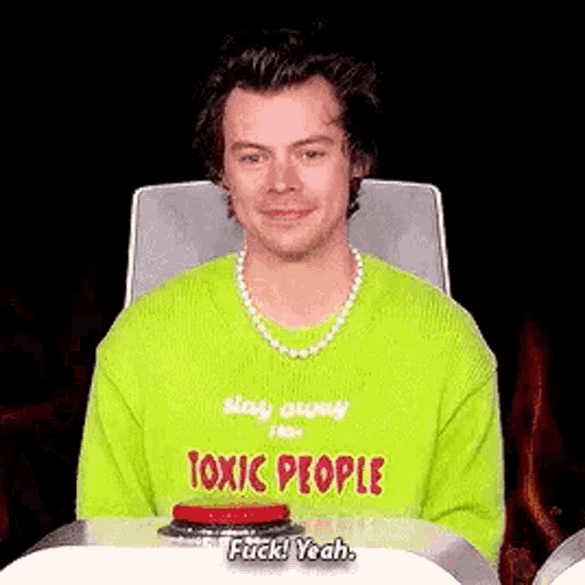 harry styles is wearing a green sweater with the words `` toxic people '' on it .