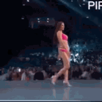a woman in a pink bikini is walking on a stage in front of a crowd