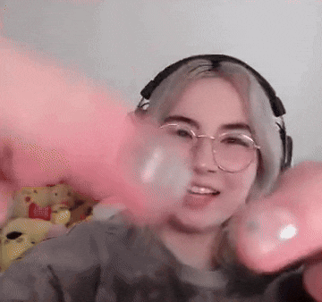 a woman wearing glasses and headphones is blowing pink balloons .
